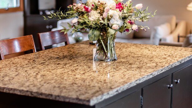 Un îlot de cuisine doté d’un plan de travail en granit, d’un vase de fleurs et de deux suspensions.