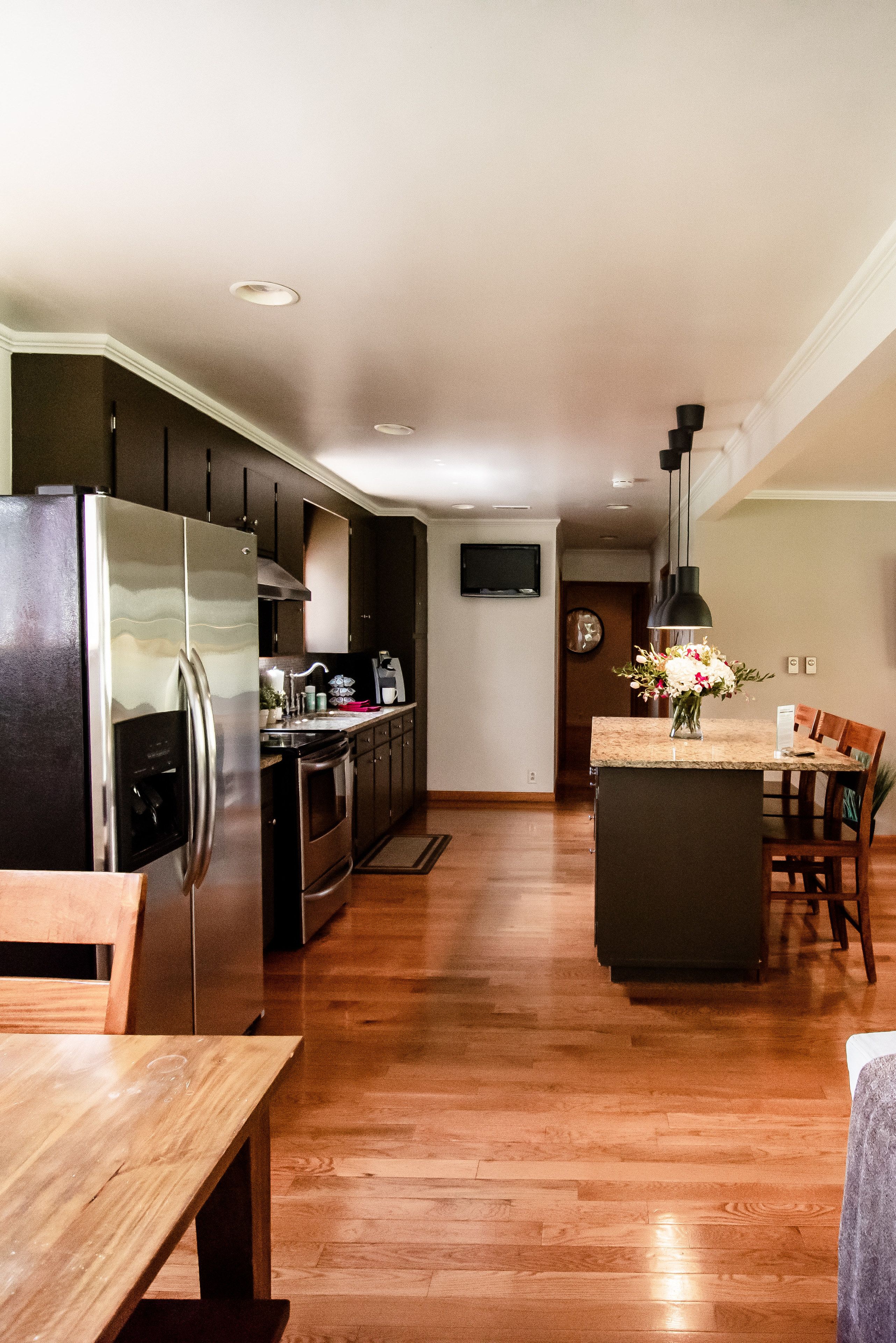 A modern kitchen with a stainless steel refrigerator, wooden cabinets, and a central island with a vase of flowers.