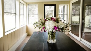 Une pièce avec une grande fenêtre, une table en bois foncé et un vase rempli de fleurs.