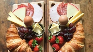 Deux planches en bois sur lesquelles sont disposés des aliments, ainsi que deux tasses de thé, le tout sur une table en bois.