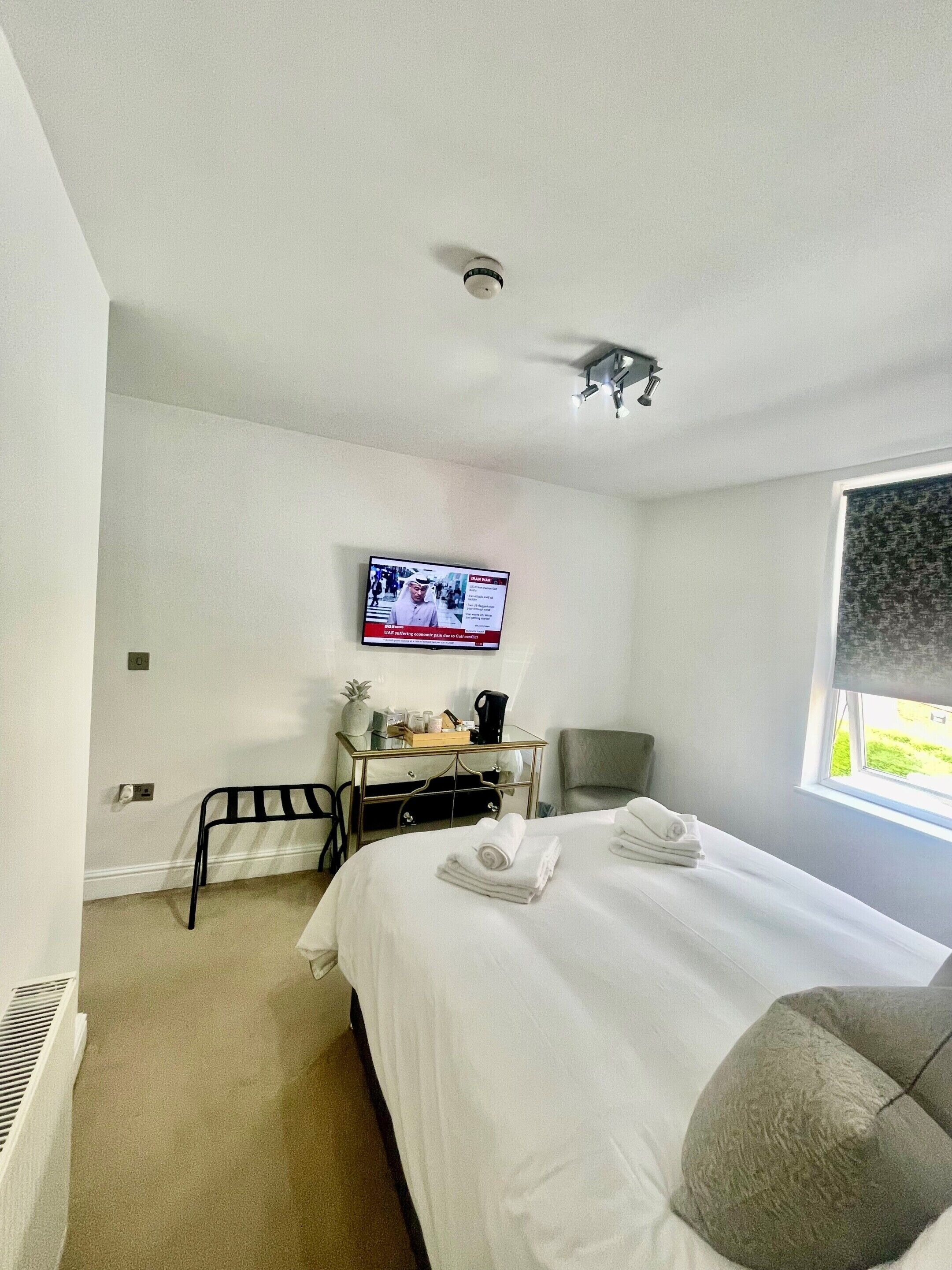 A hotel room with a bed, a desk with a computer, a chair, a TV mounted on the wall, and a window.