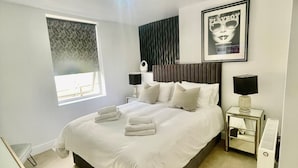 Une chambre d’hôtel moderne avec un grand lit, des tables de chevet, un radiateur et une fenêtre avec des stores.