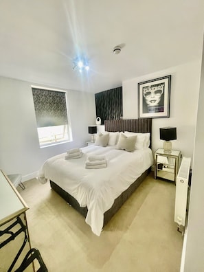 A modern hotel bedroom with a large bed, bedside tables, a radiator, and a window with blinds. - Jasmine House Bed & Breakfast (Lutterworth)