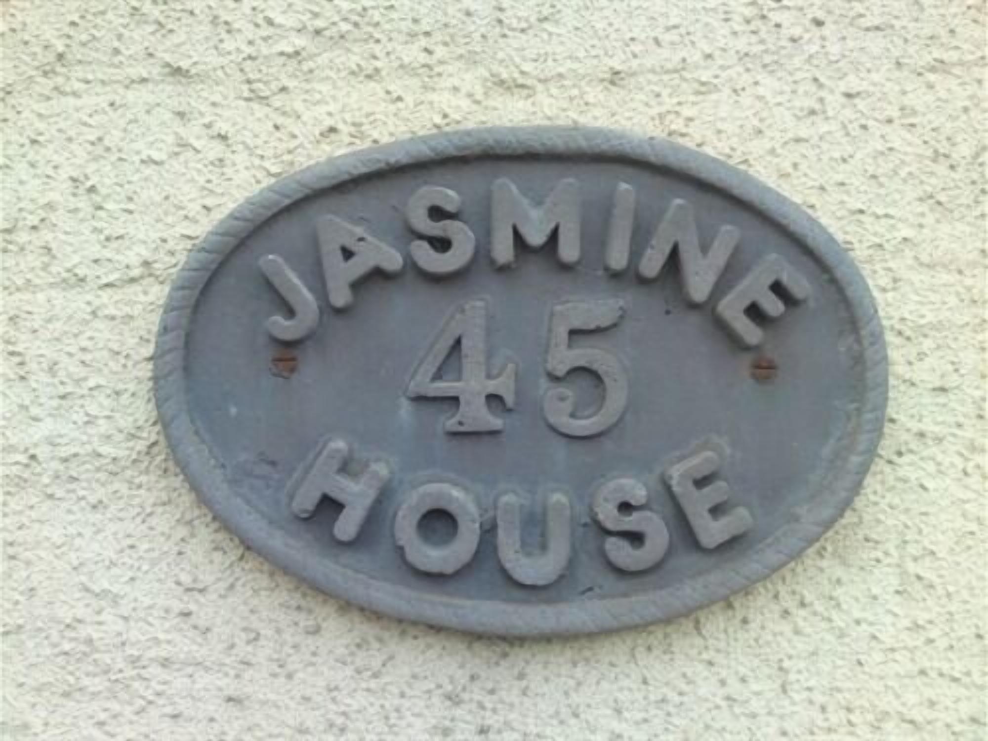 Una placa con el número de casa que dice 'JASMINE 45 HOUSE' sobre una pared con textura.