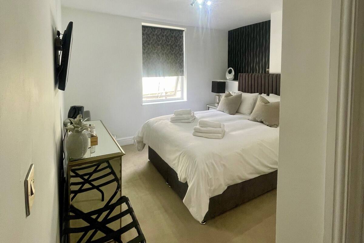 Un dormitorio con cama, mesita de noche, lámpara y ventana.