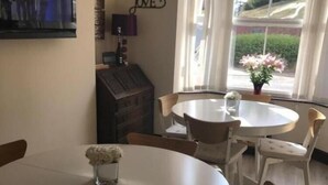 Un coin repas avec deux tables rondes, chacune entourée de quatre chaises. Un panneau décoratif est accroché au mur, sur lequel on peut lire : « VIVEZ, RIEZ, AIMEZ ».