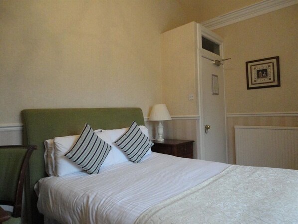 A neatly made bed with white linens and striped pillows, a green headboard, and a small bedside table with a lamp.