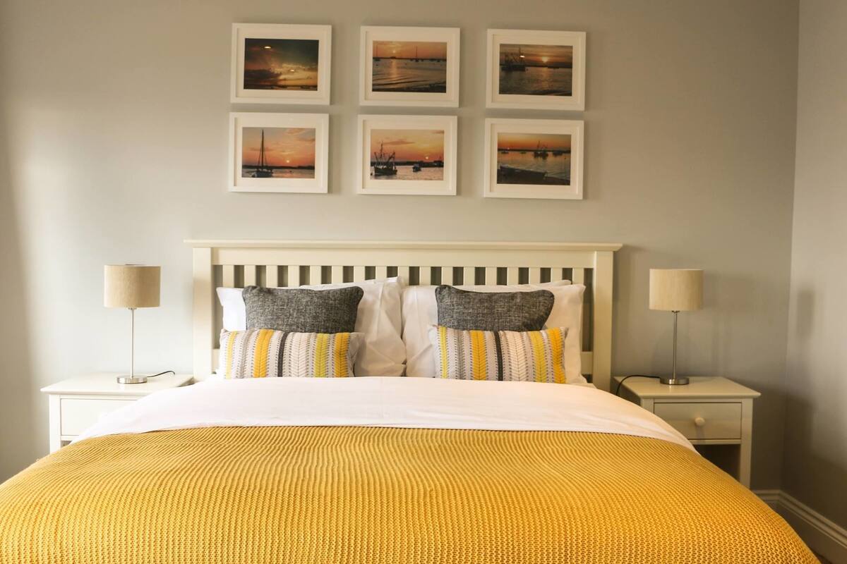 A neatly arranged bedroom with a bed, two bedside tables, and four framed pictures on the wall.