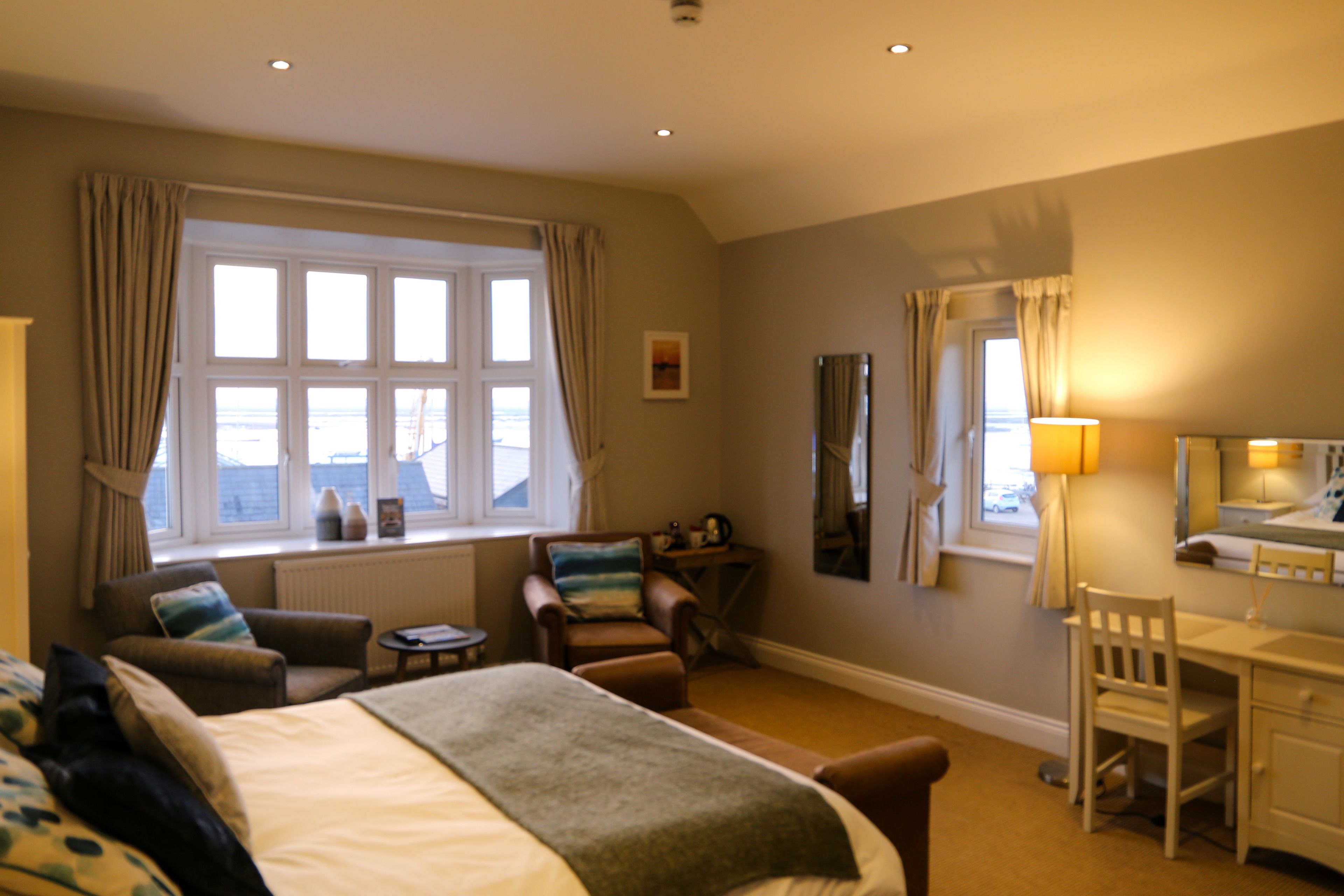 A hotel room with a bed, two armchairs, a desk, and a window with curtains.