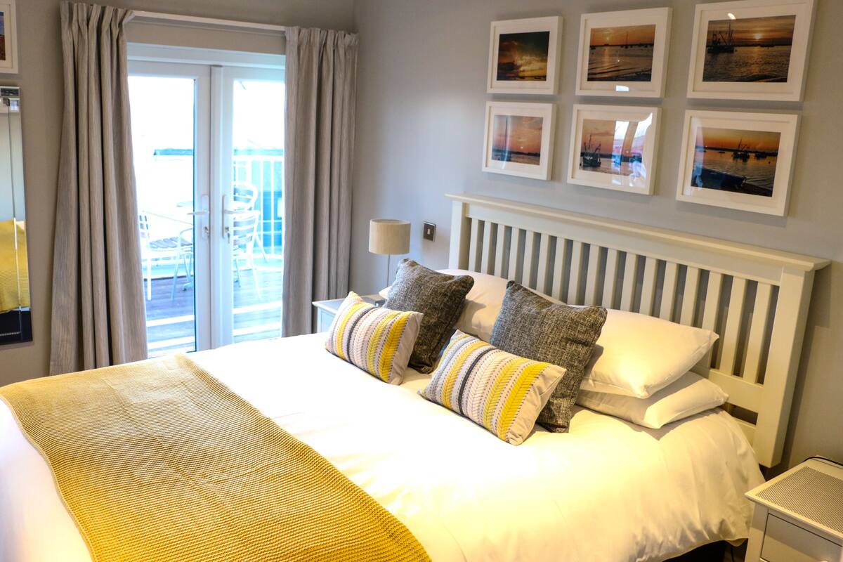 A hotel room with a large bed, a view of the balcony, and several framed pictures on the wall.