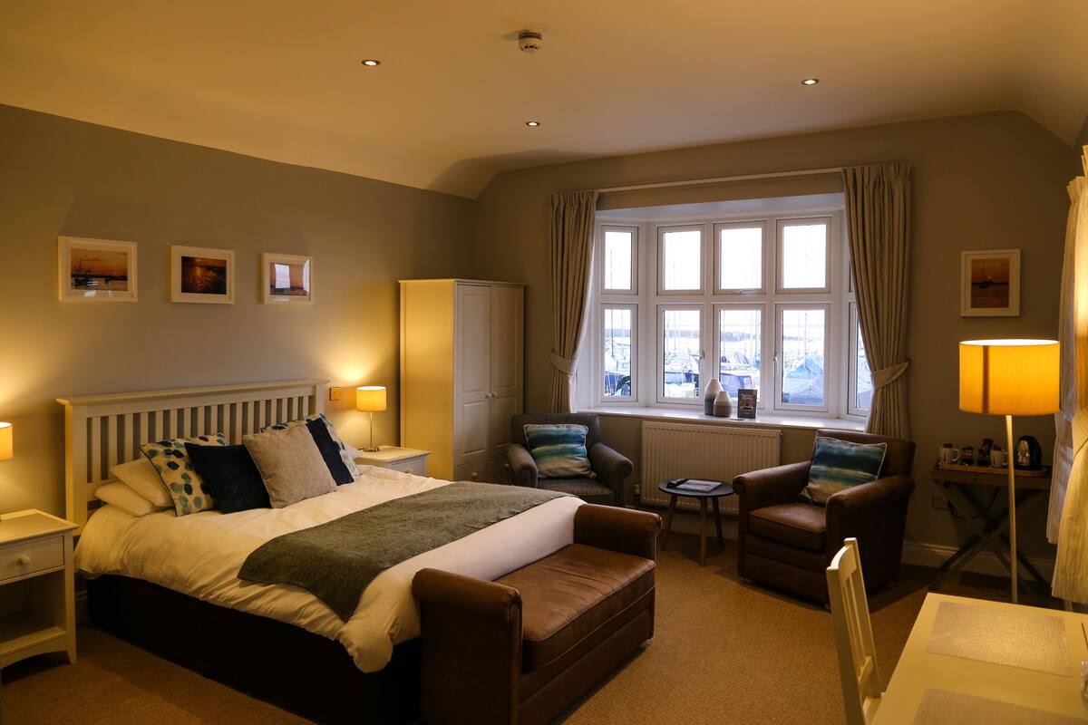A hotel room with a large bed, two armchairs, a small table, and a window with curtains.