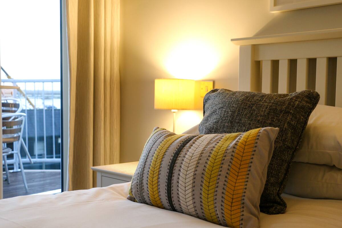 A hotel room with a bed, a nightstand with a lamp, and a view of the outside balcony.