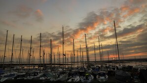 Un puerto deportivo con varios veleros amarrados, un atardecer de fondo y cielo despejado.