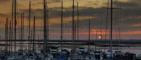Un port de plaisance où sont amarrés de nombreux bateaux, un coucher de soleil en arrière-plan et une surface d'eau calme.