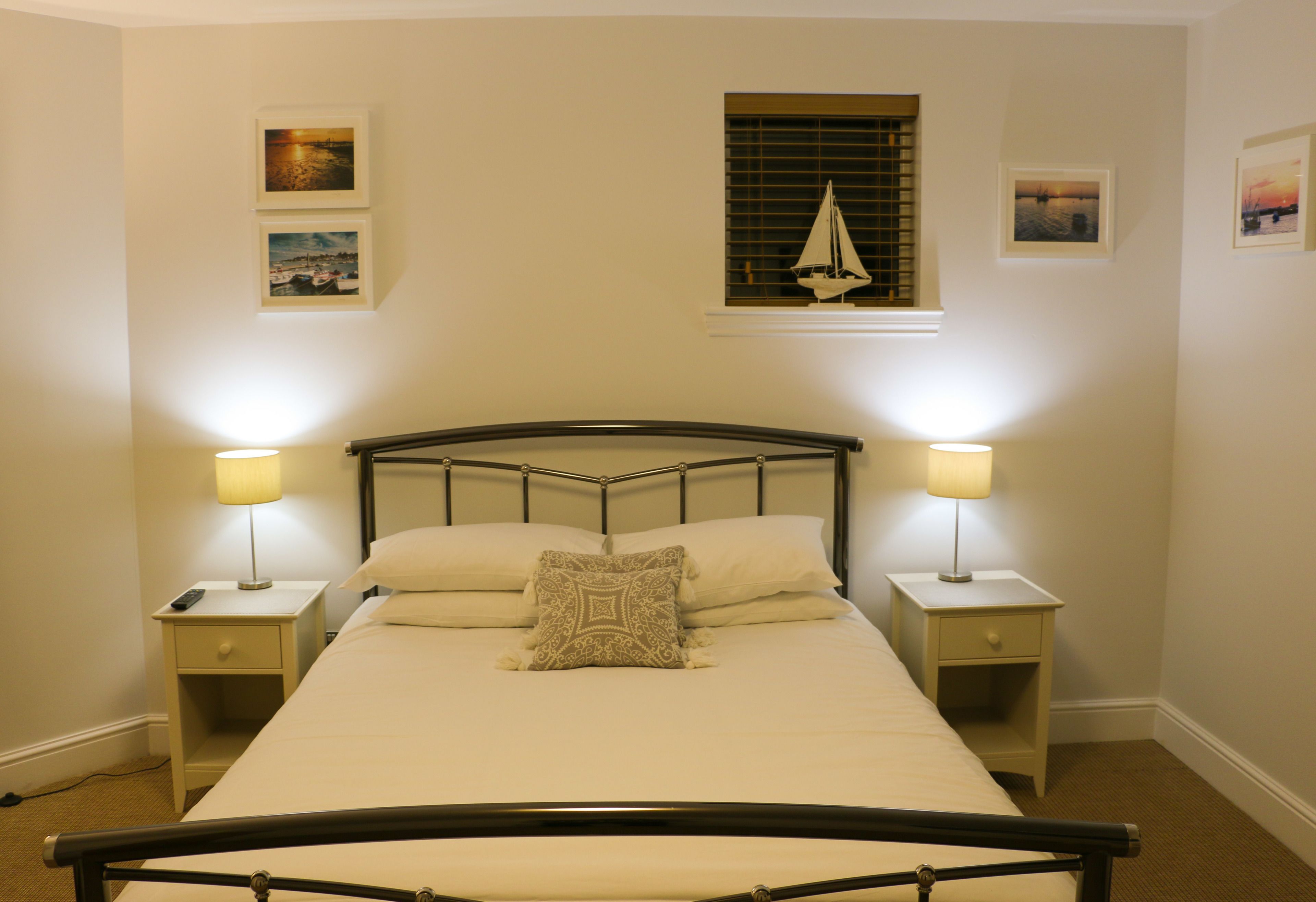 A neatly made bed with a headboard, two bedside tables with lamps, and framed pictures on the walls.