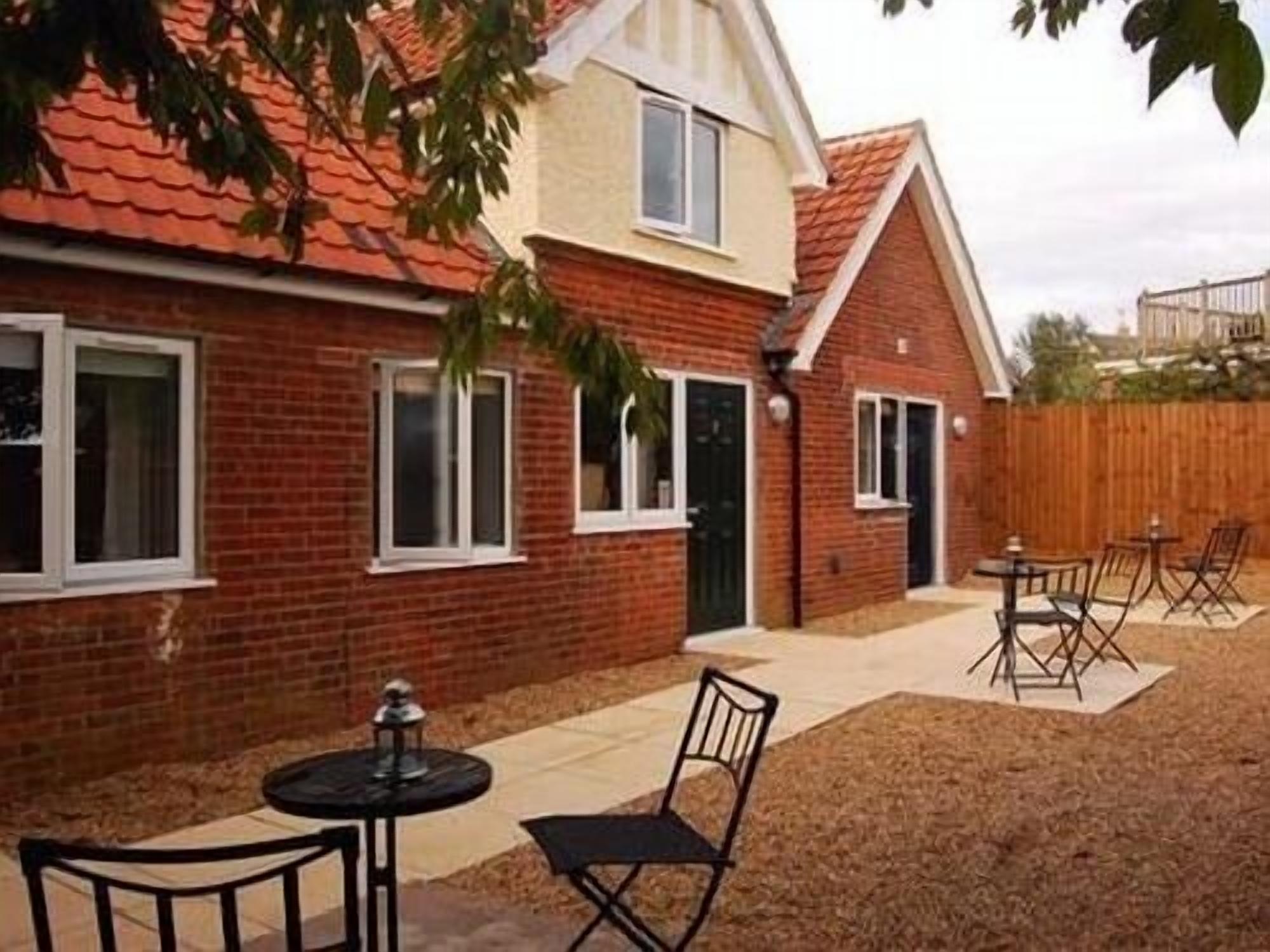 A two-story brick house with a tiled roof, a fenced backyard, and outdoor seating.
