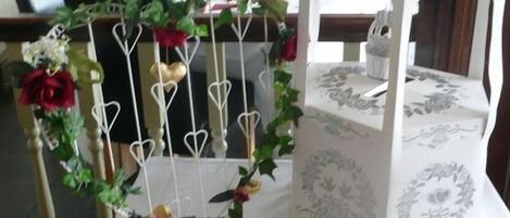 Uma mesa com toalha branca, um livro vermelho e um candeeiro branco com padrão floral.