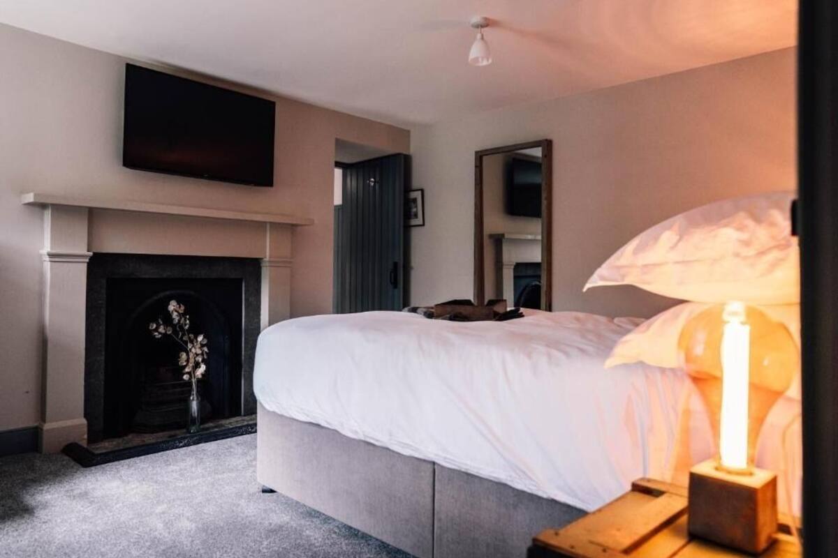 A bedroom with a bed, a fireplace, a TV mounted on the wall, and a bedside table with a candle.