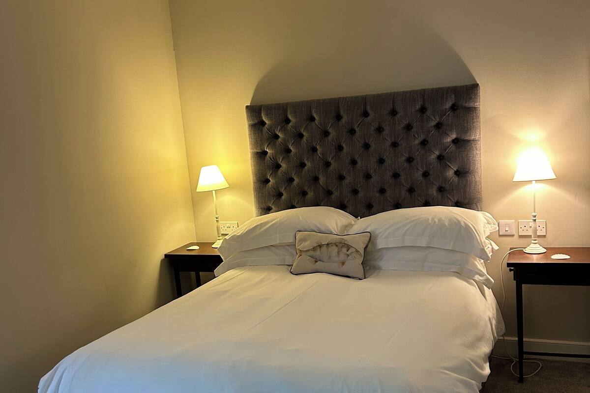 A neatly made bed with a tufted headboard, two bedside tables with lamps, and a carpeted floor.