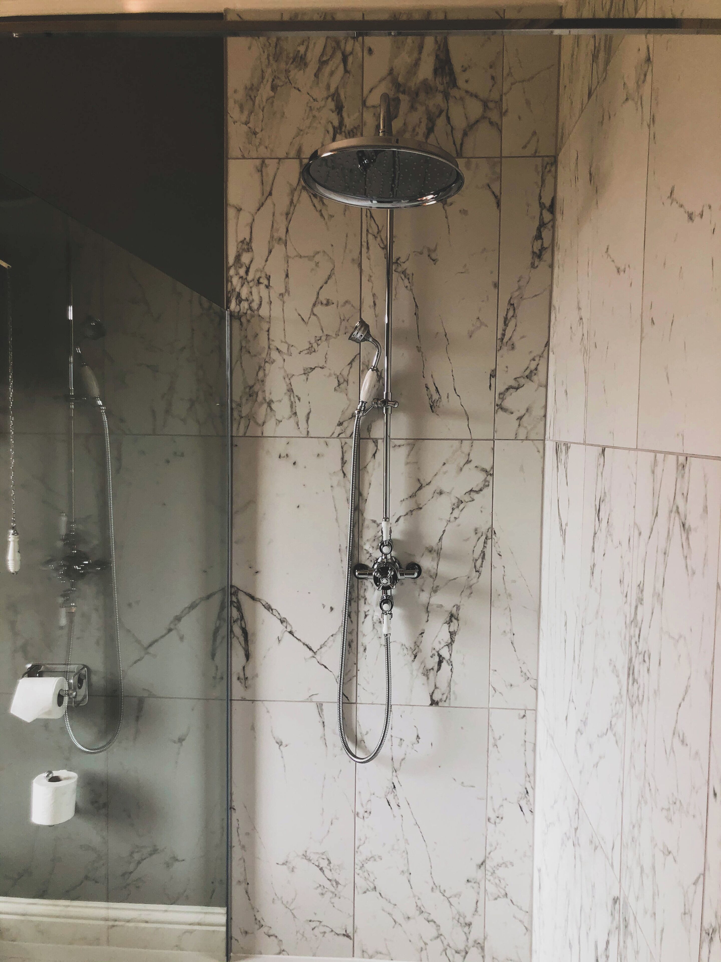 A shower with a handheld showerhead and a wall-mounted control.