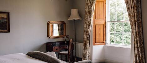 A bedroom with a large bed, a desk, a chair, a lamp, and a window with curtains.
