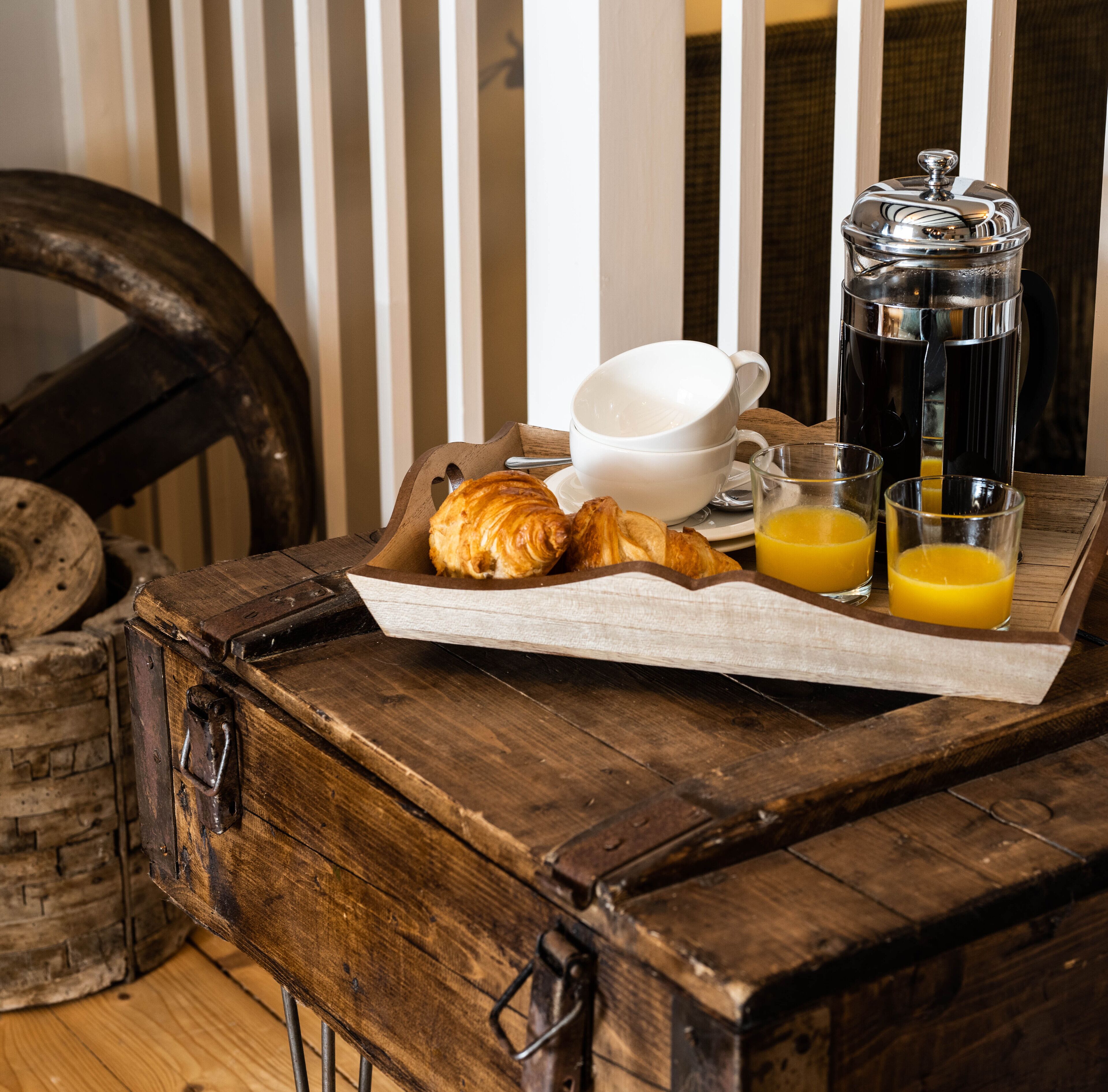 A wooden table with a tray containing croissants, a coffee pot, a cup, and glasses of orange juice.
