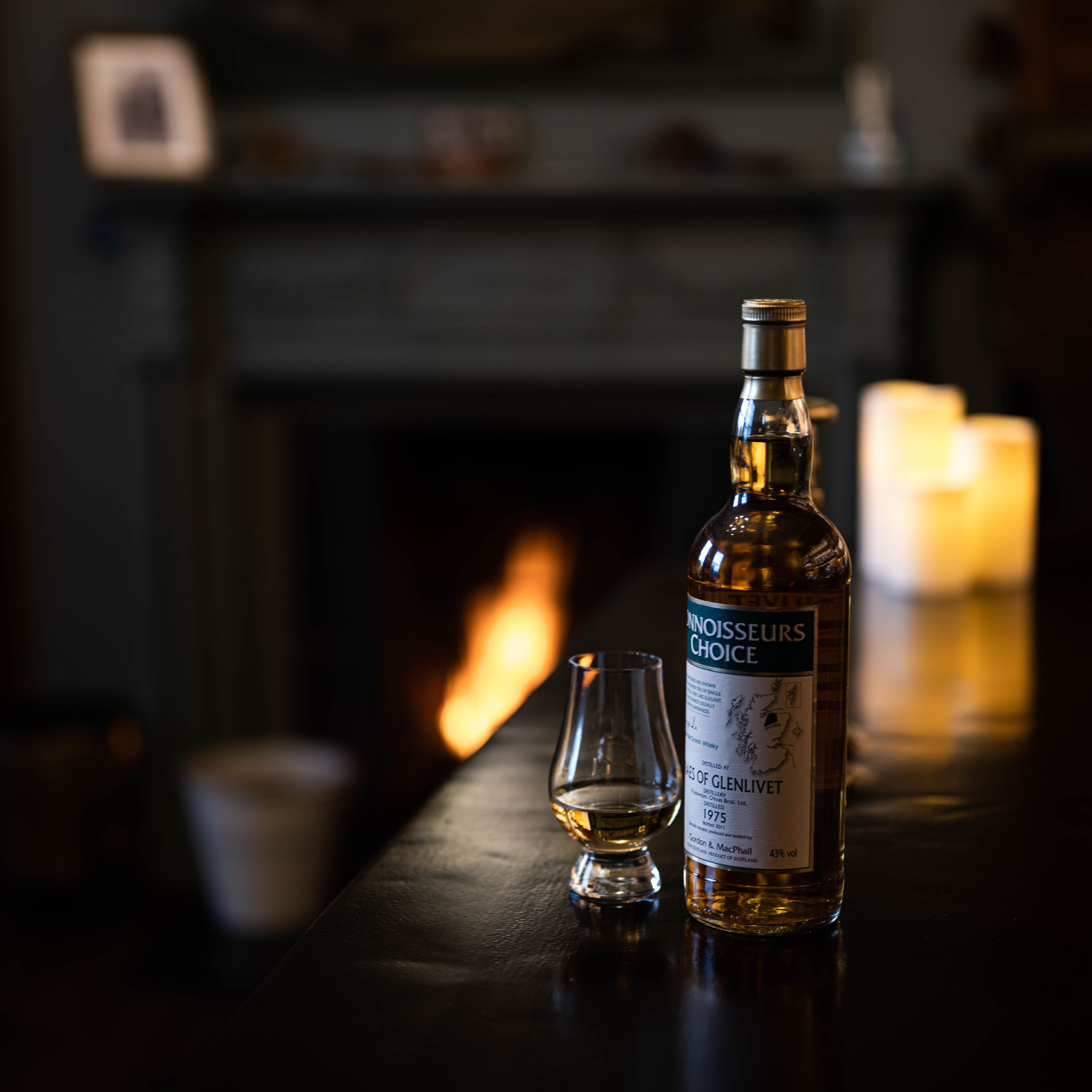 Eine Flasche Whisky und ein Glas auf einer Bartheke, im Hintergrund ein Kamin.