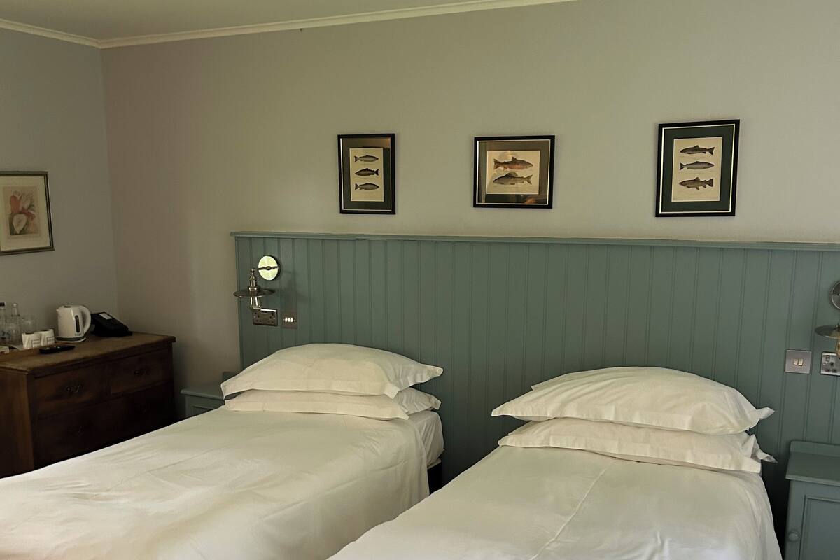 A room with two single beds, a wooden dresser, a mirror, and framed fish pictures on the wall.