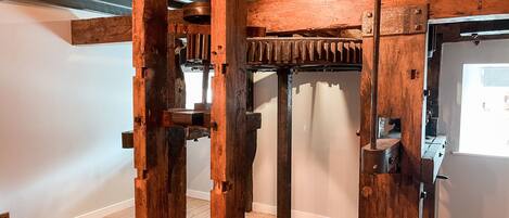 Una habitación con vigas de madera a la vista, un gran mecanismo y una puerta con ventanal.