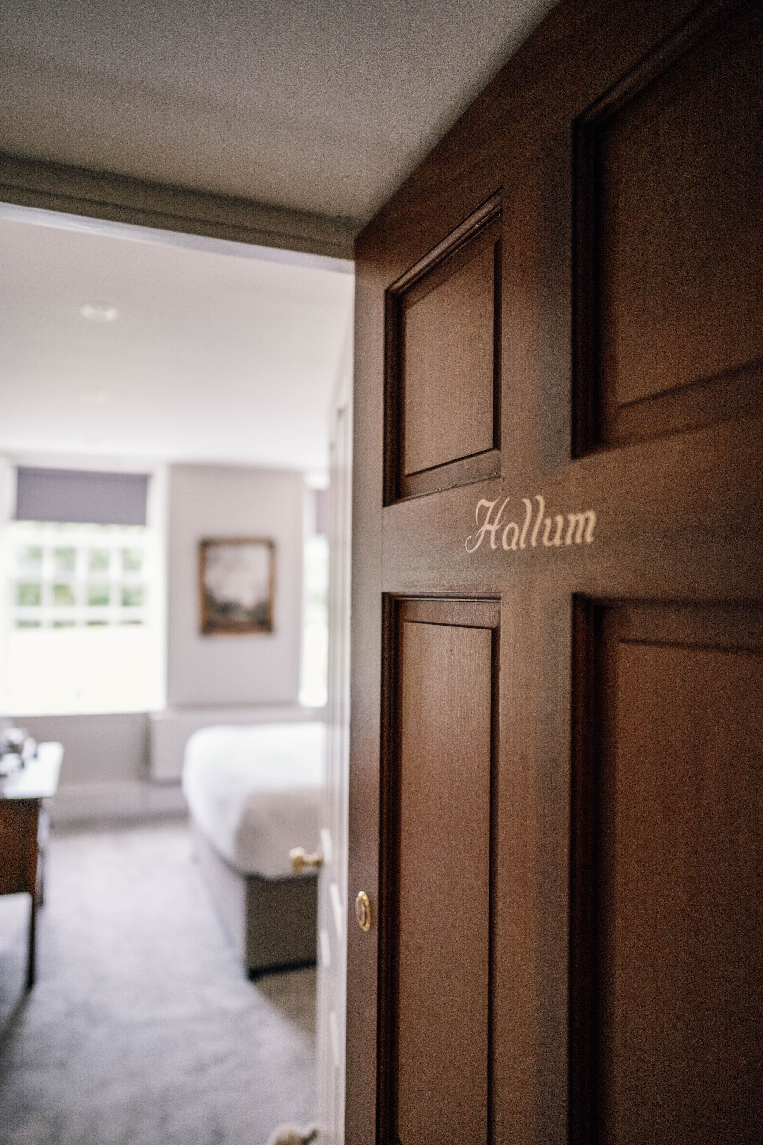Una puerta de madera con el nombre "Hallum" grabado, que da paso a un dormitorio con una cama y una ventana.
