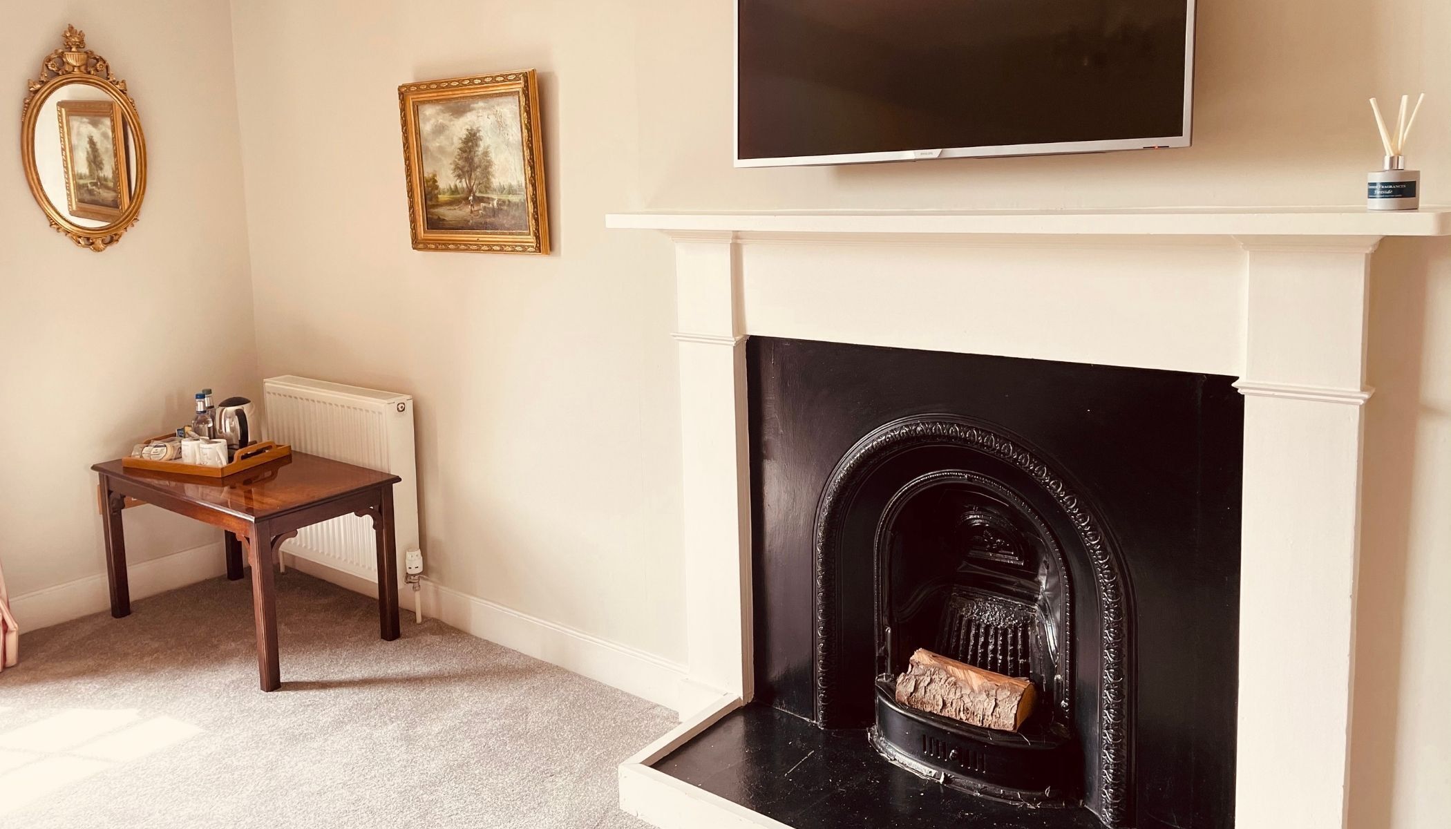 Una sala de estar con una chimenea negra, un televisor encima y dos cuadros en la pared.