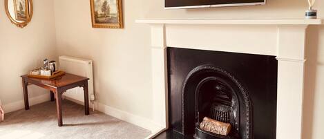 Una sala de estar con una chimenea negra, un televisor encima y dos cuadros en la pared.