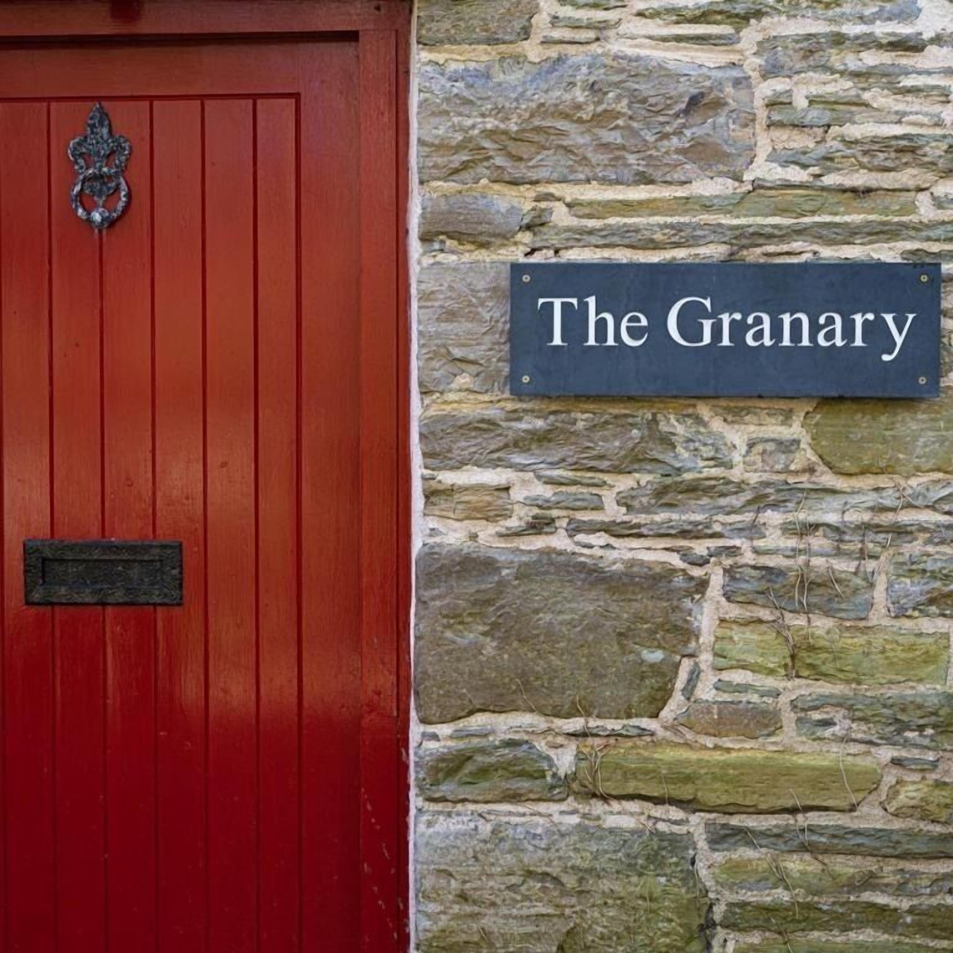 A red door with a metal knocker and a stone wall with a sign reading "The Granary".