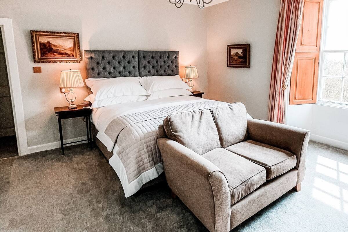 A bedroom with a bed, two bedside tables with lamps, a sofa, and a window with curtains.