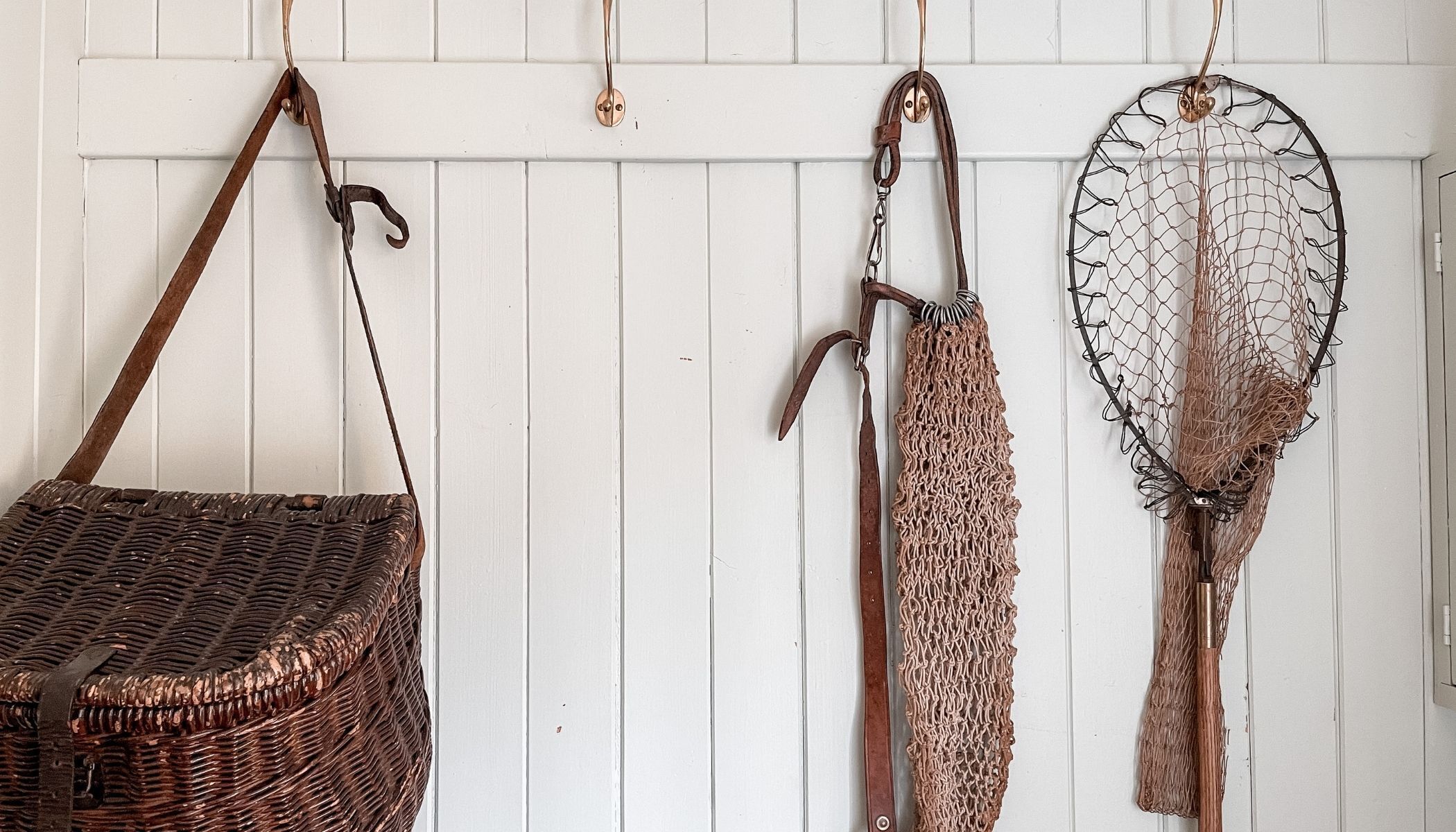 A wicker basket, a metal tool, and a net hanging on a white wall.