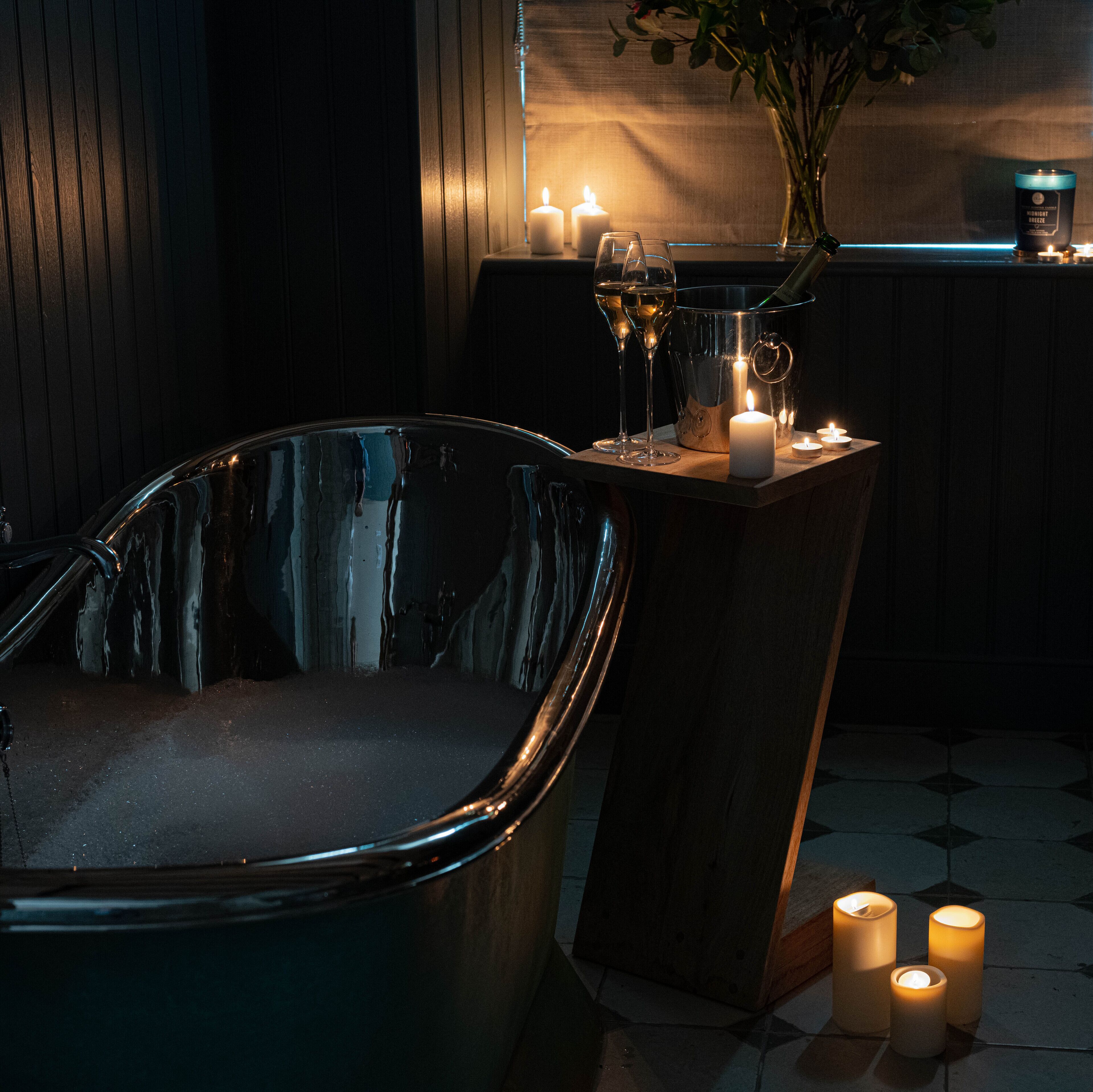 Een kamer met weinig licht, een groot helder bad, een tafeltje met kaarsen en een vaas met bloemen.