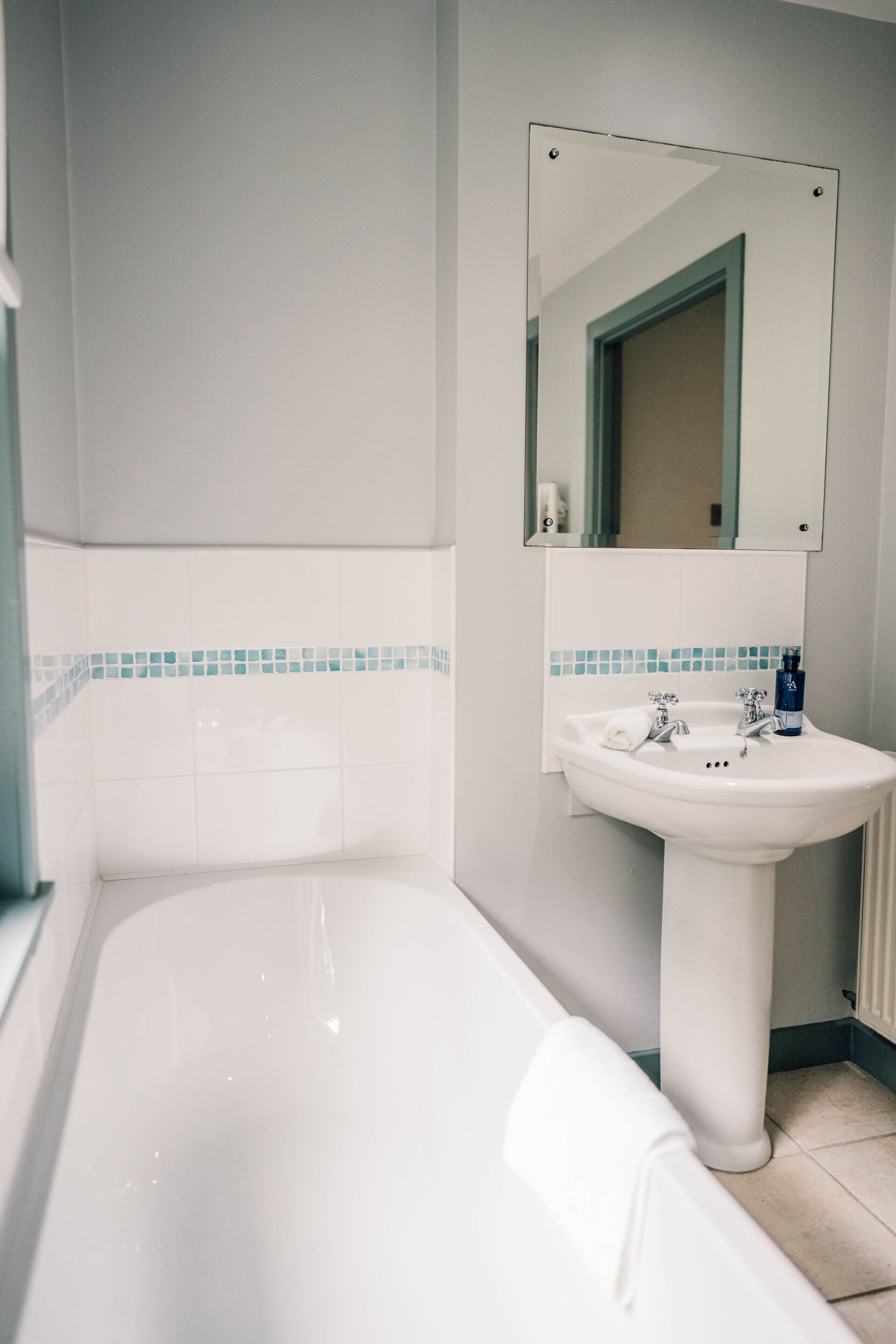 Un baño con una bañera blanca, un lavamanos con espejo arriba y un borde de azulejos azules a lo largo de la pared.