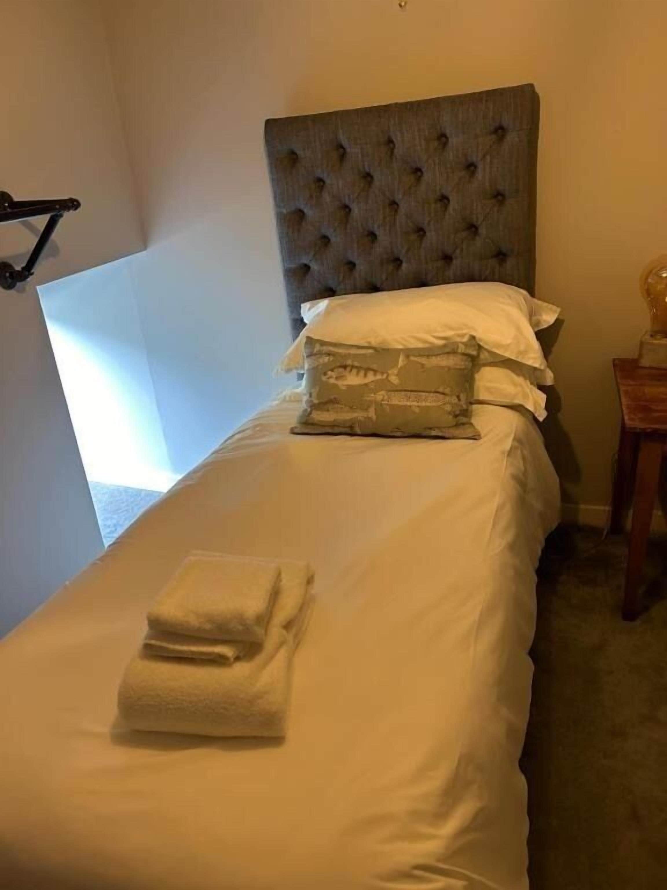 A single bed with a tufted headboard, white bedding, and a folded towel.