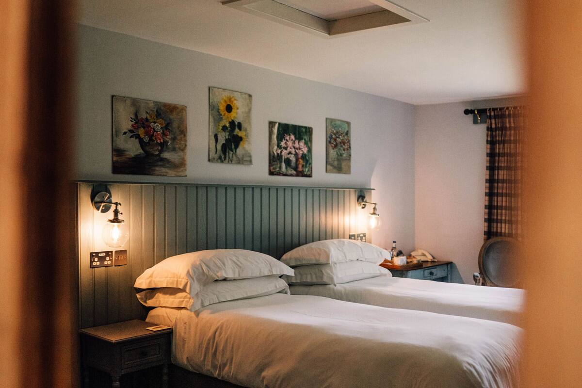 A bedroom with two beds, a nightstand, a chair, and wall-mounted artwork.