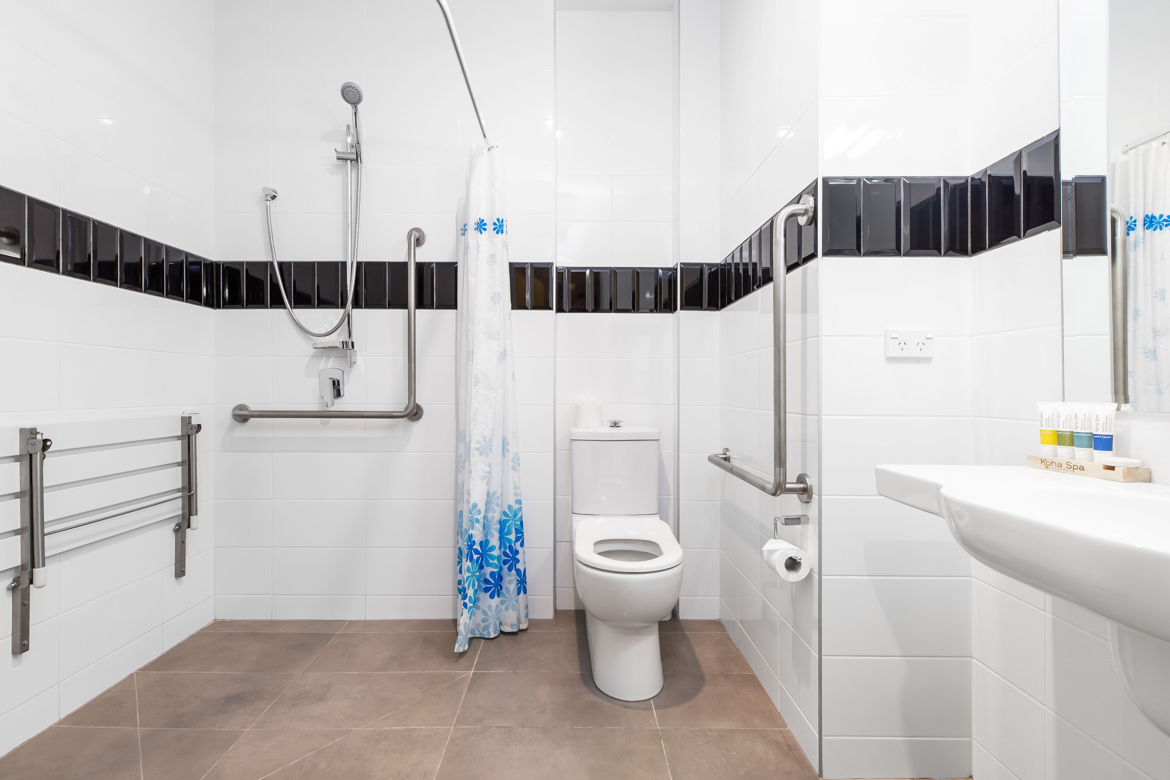 Et moderne badeværelse med toilet, bruser og gelændere.