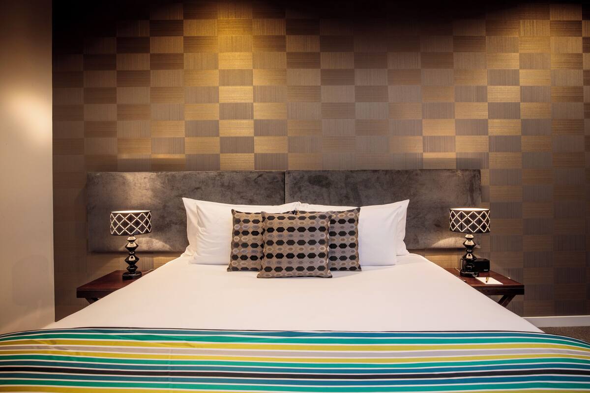Un lit bien fait, avec une couvre-lit à rayures, deux lampes de chevet et un coussin à motifs.