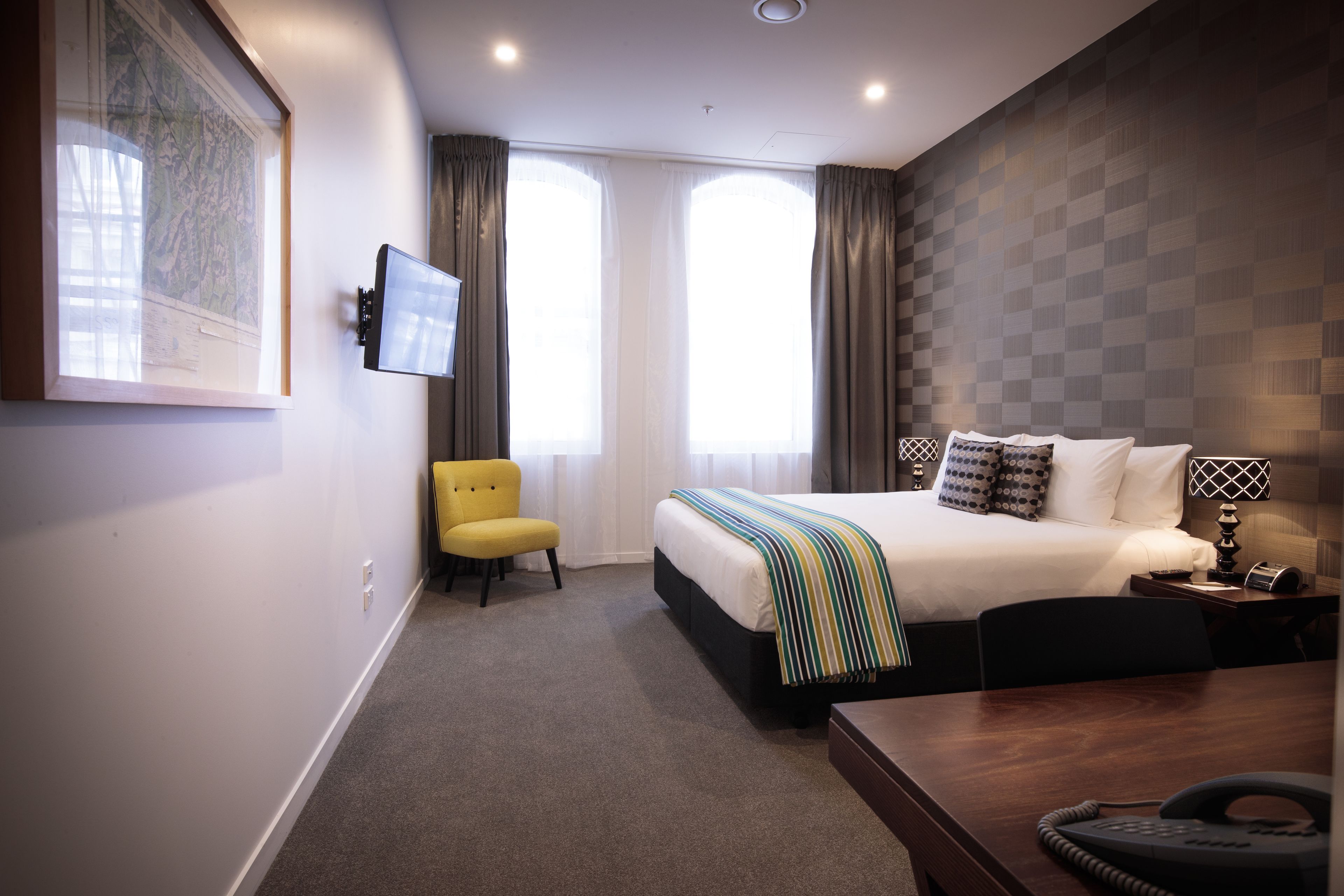 A hotel room with a bed, a desk, a chair, a TV, and a window with curtains.