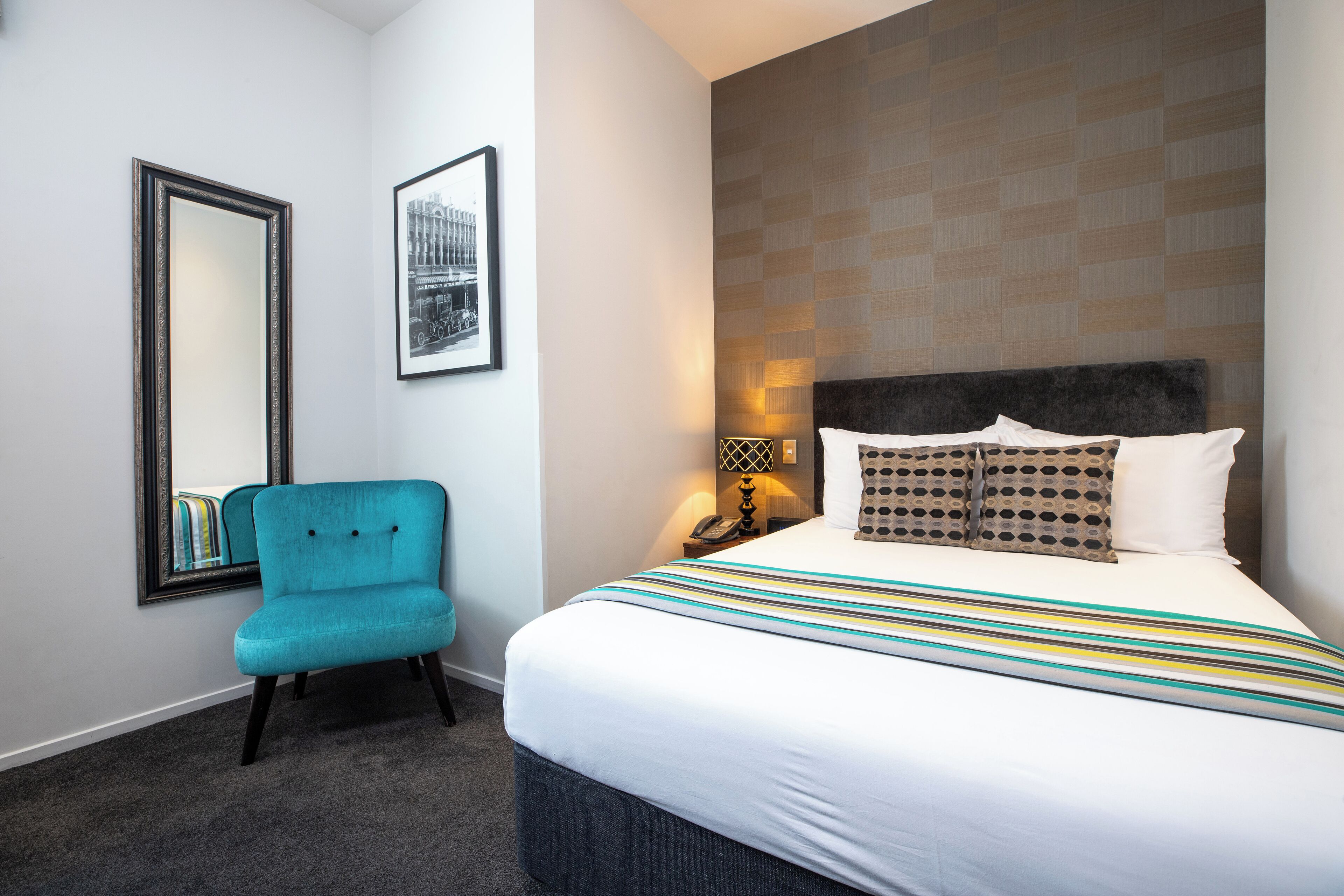 Ein Hotelzimmer mit einem großen Bett, einem blauen Sessel, einem gerahmten Bild an der Wand und einer Wand mit Muster.