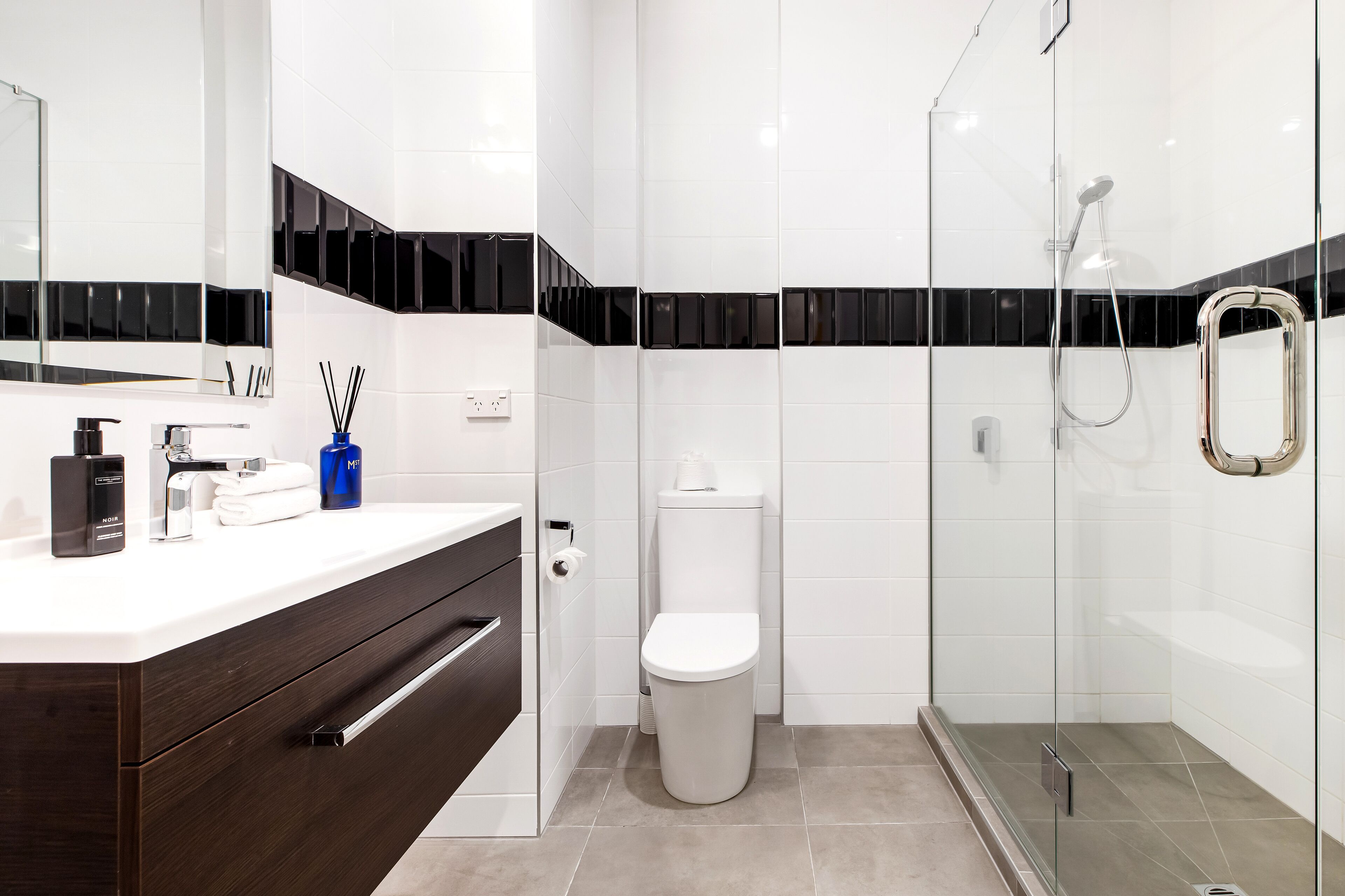 A modern bathroom with a white vanity, a toilet, and a glass-enclosed shower area.