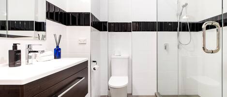 A modern bathroom with a white vanity, a toilet, and a glass-enclosed shower area.