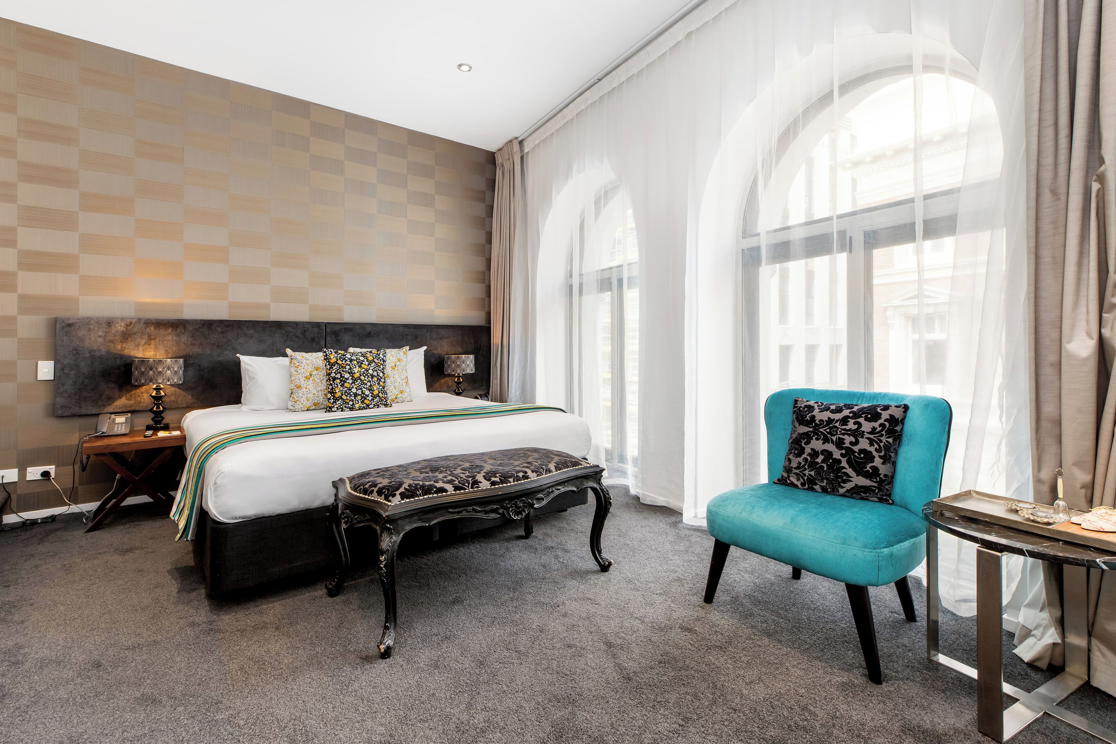 A hotel room with a large bed, a small table, a chair, and a window with curtains.