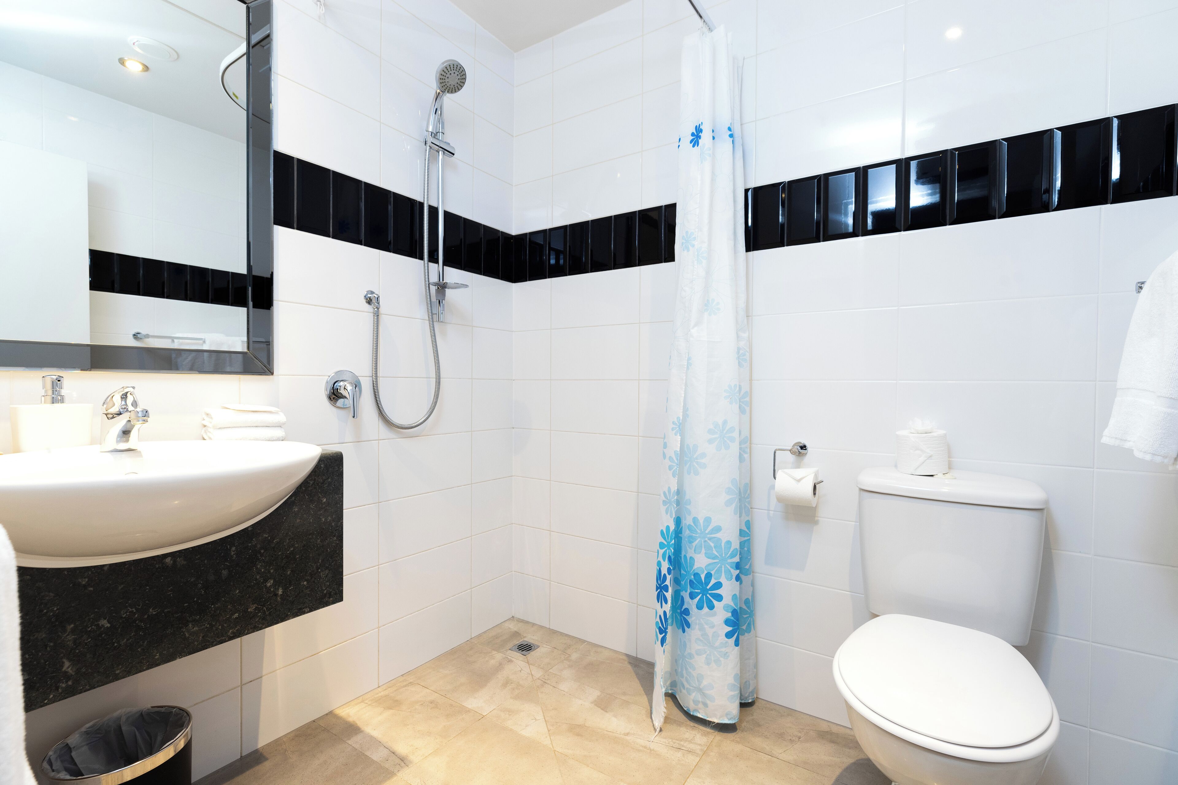 Et badeværelse med en hvid vask, bordplade i sort og brusebad samt toilet.