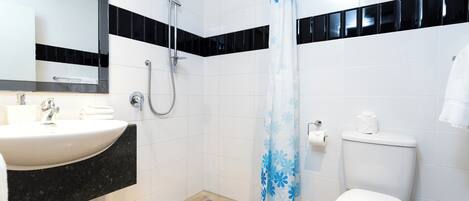 A bathroom with a white sink, black countertop, shower, and toilet.