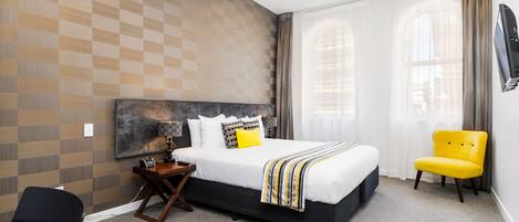 A modern hotel room with a large bed, a desk, and a chair.