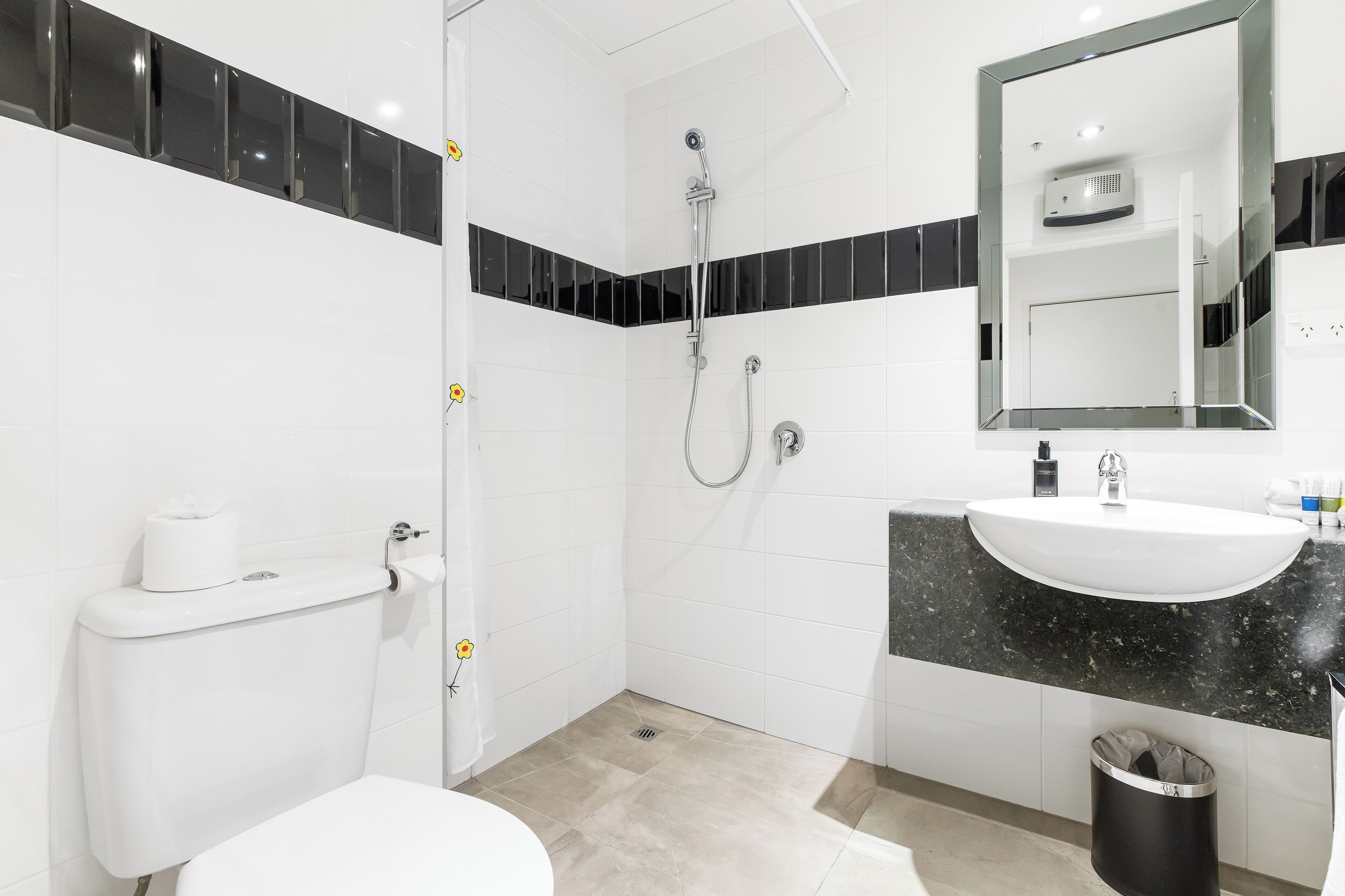 Un baño moderno con inodoro, ducha, lavamanos y un cubo de basura.